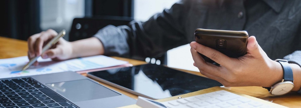 Vrouw met een pen en een telefoon in haar hand berekent financiële zaken achter een latop