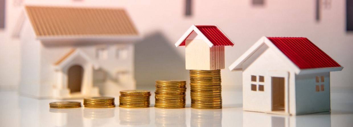 stapeltjes geld die steeds hoger worden met op de achtergrond huizen