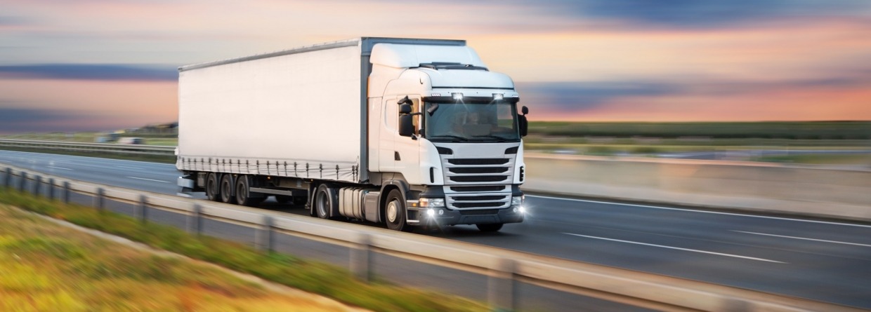 Een witte vrachtwagen onderweg op de grote weg bij ondergaande zon