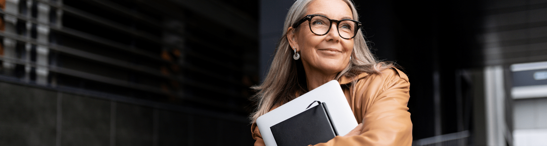 Een dame met bril staat buiten kantoor met een laptop in haar handen